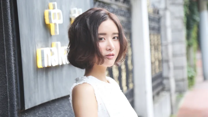 一位留着短发的成年女性站在城市建筑外墙旁。