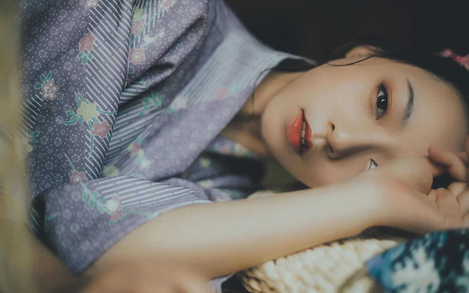 성인 여성이 무늬가 있는 천 위에 옆으로 누워 가까이에서 카메라를 바라보고 있다.
