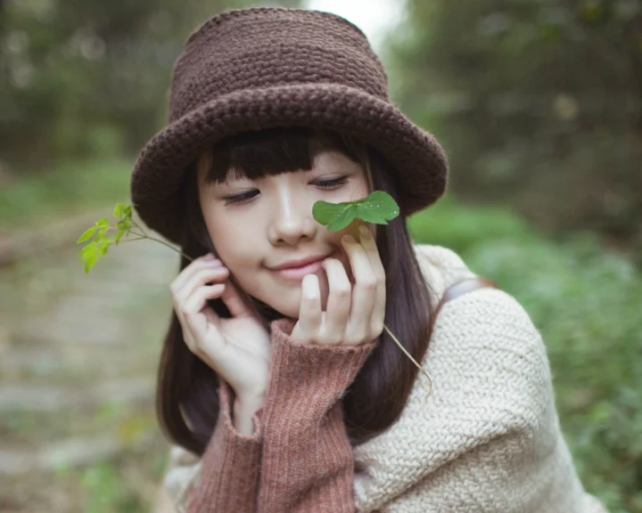 一位戴着棕色针织帽的女性在森林中手持叶片靠近脸庞。