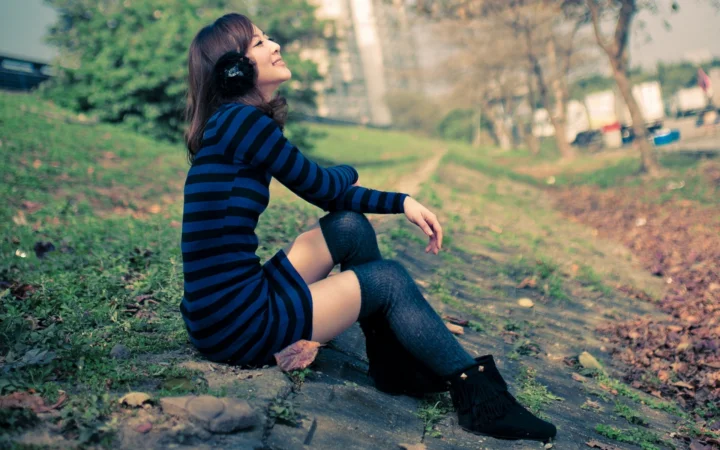 一名穿条纹连衣裙和长袜的女子坐在公园小路旁。