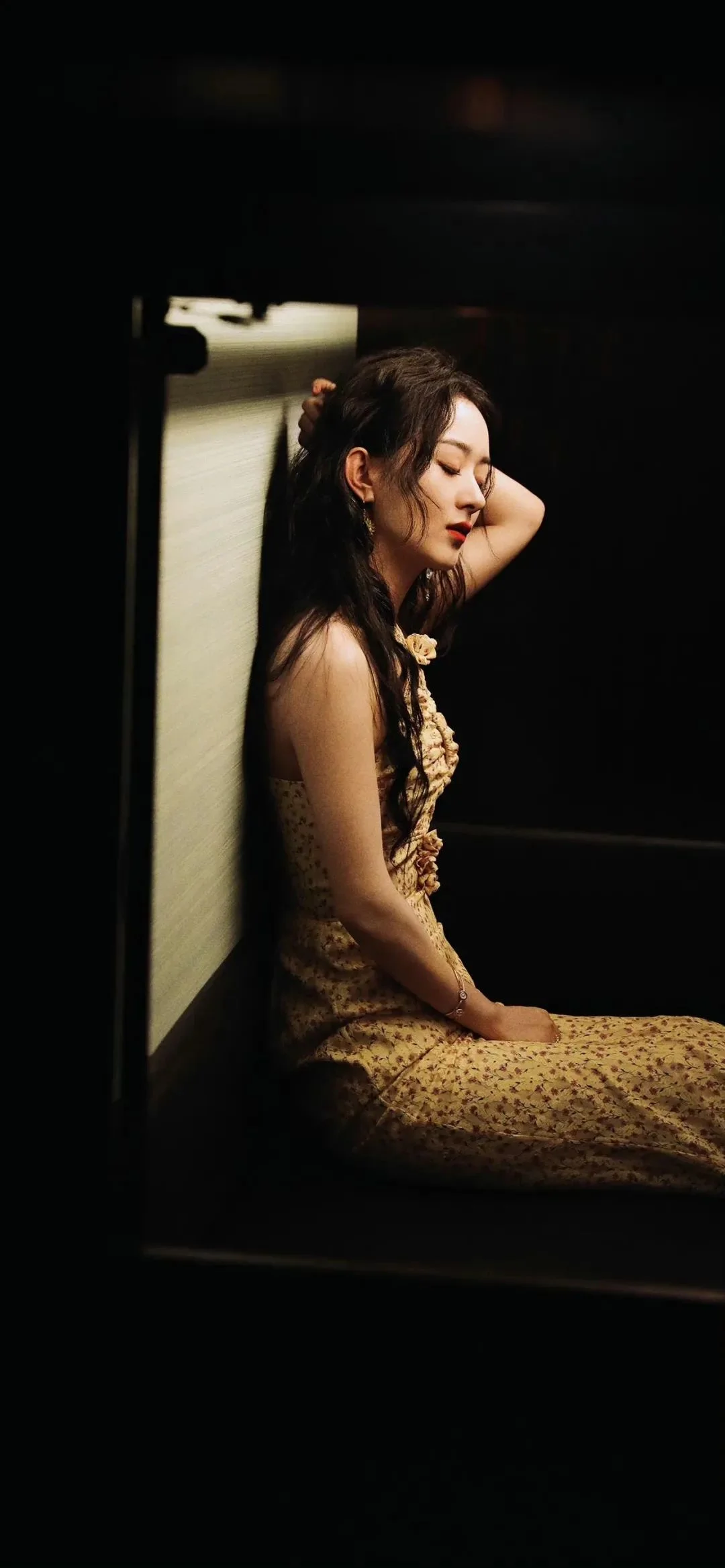 柄のあるワンピースを着た成人女性が、暗い室内の椅子に座っています。