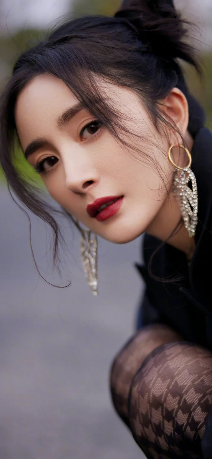 一名成年女性身穿黑色服装，佩戴醒目的长耳环，以近距离侧倾姿态面对镜头。