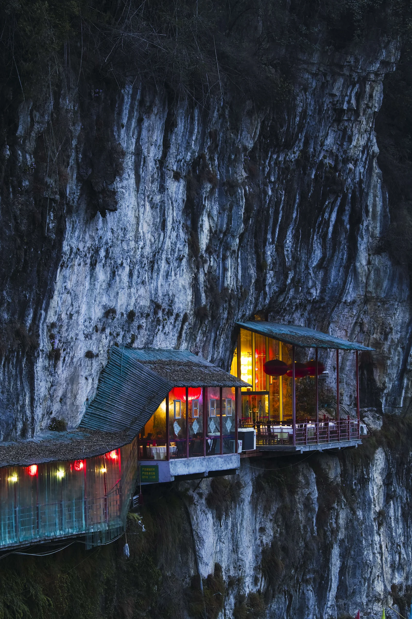 陡峭岩壁上的临崖小屋在夜色中亮起温暖灯光。