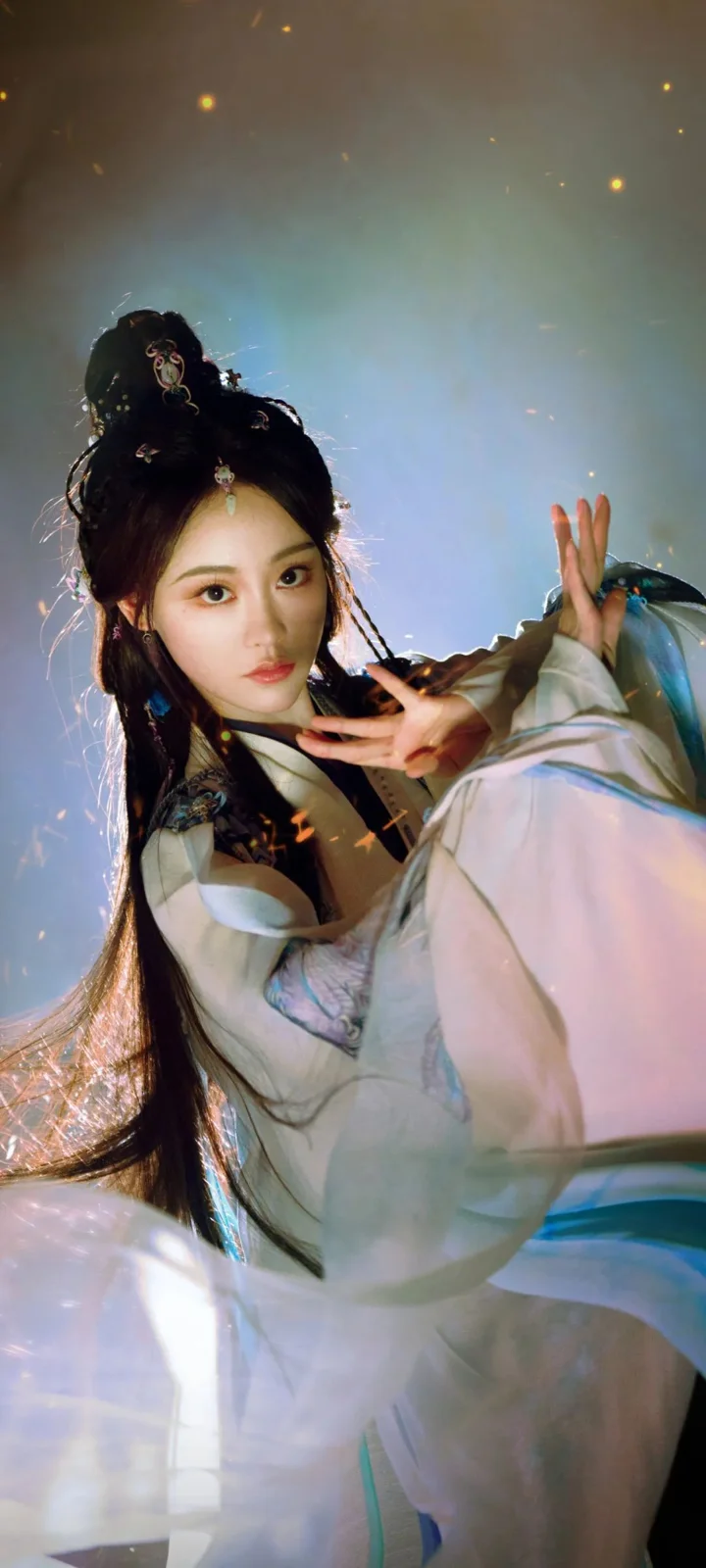 一位长发女性身穿浅色飘逸服装，置身于蓝色发光背景前。