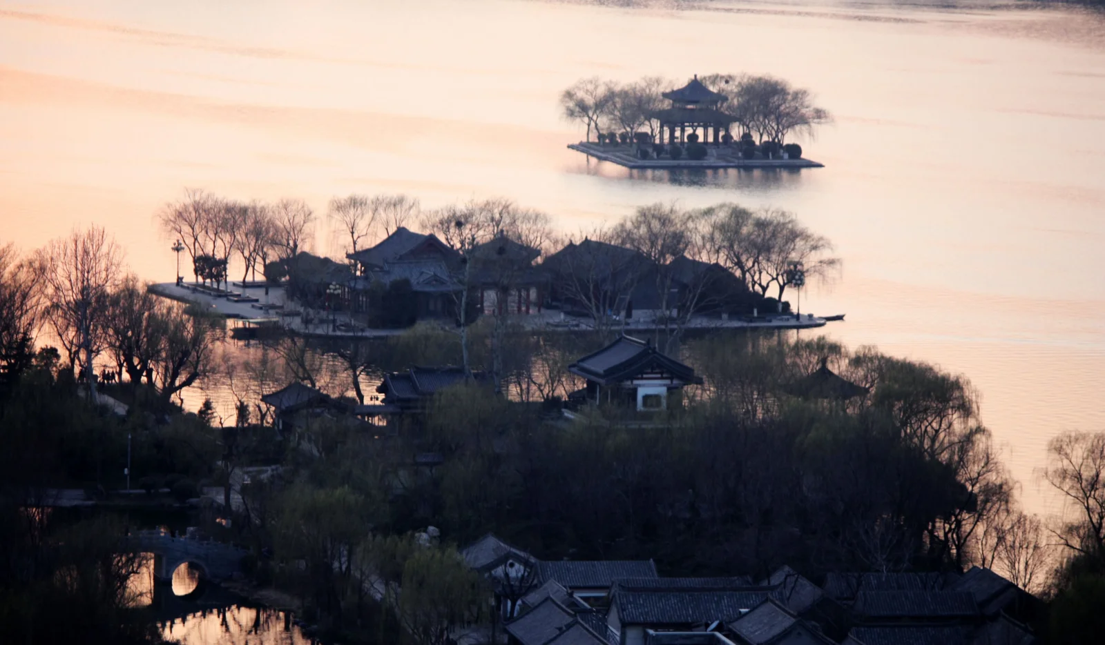 暖かな光が湖面や木々、緑の島々に点在する中国風の建物と東屋を照らしている。