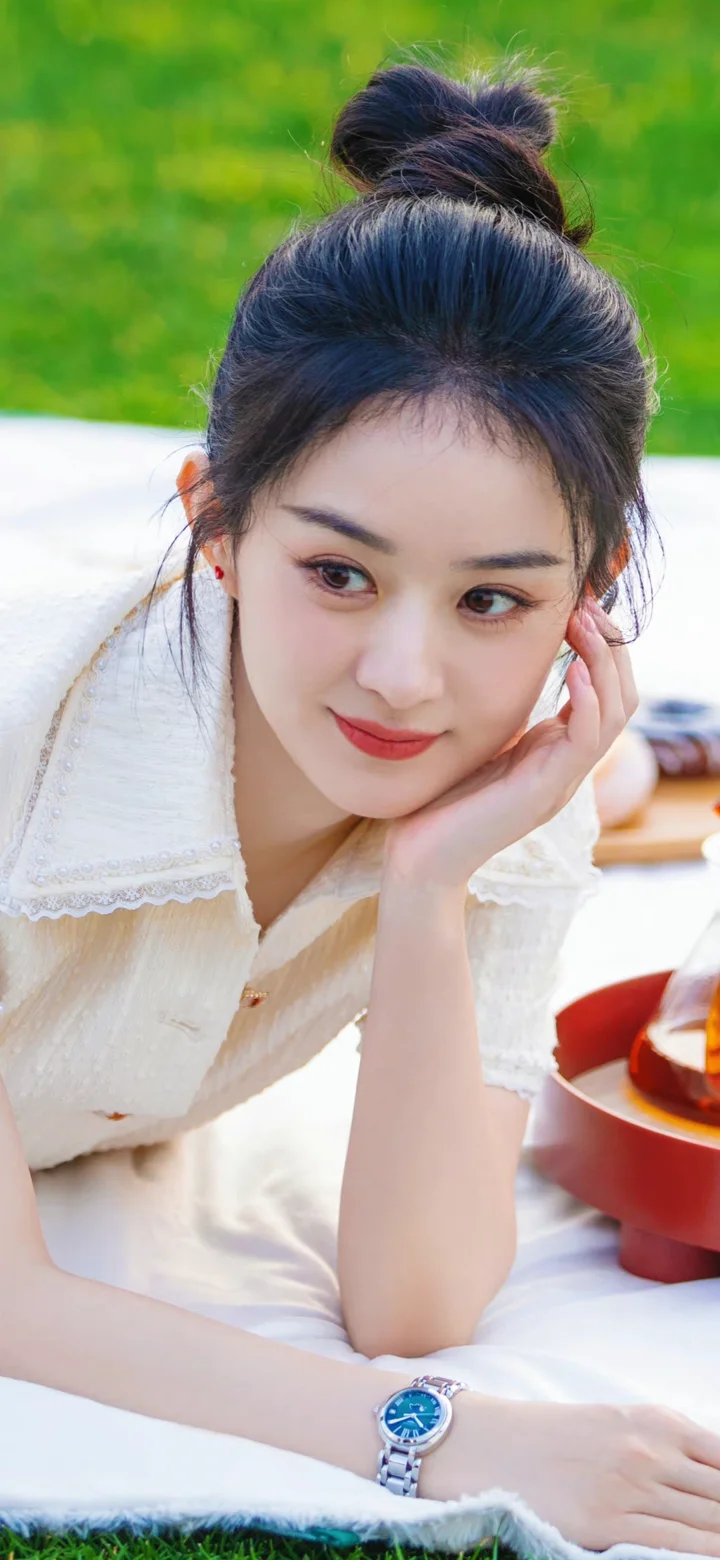 一名身穿白色上衣的女子托腮躺在户外的白色毯子上。