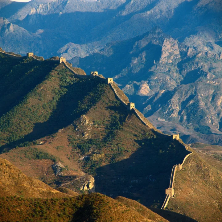长城蜿蜒穿过群山与山谷，远处是层叠的岩壁和山脉。