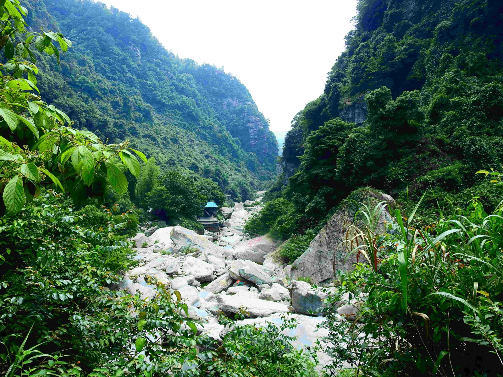 藍天白雲下，層疊的綠色山峰與雄偉的岩壁構成壯麗的自然風景。