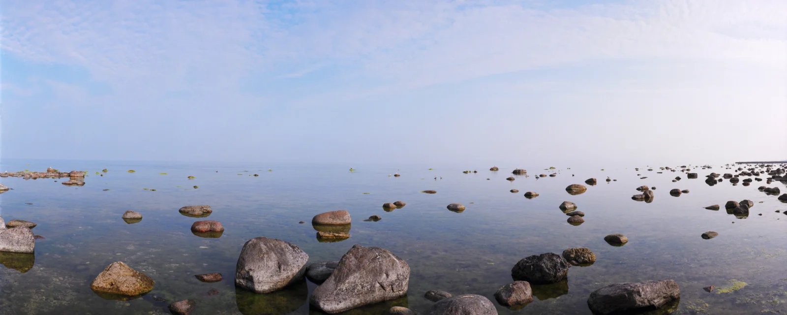 平静的海水延伸至远方，前景散布着大小不一的岩石，天空明亮开阔。