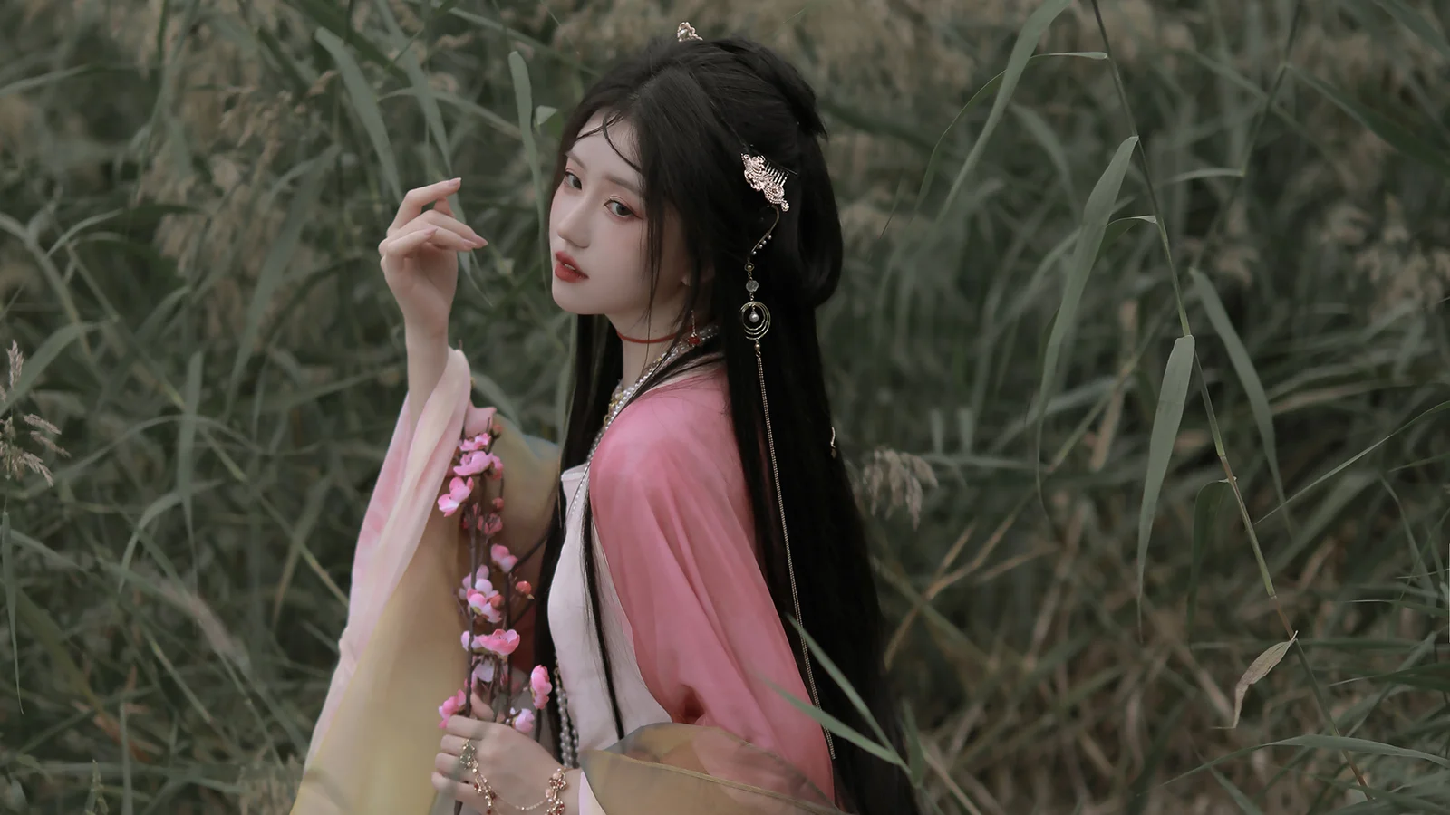 분홍색 전통 의상을 입은 여성이 갈대밭에 서 있다.
