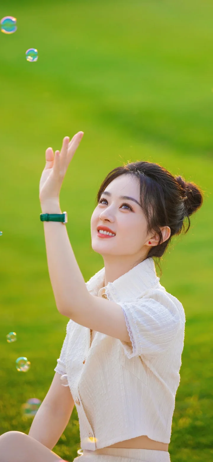 一名身穿白色上衣的女子在绿色户外背景前抬手仰望。