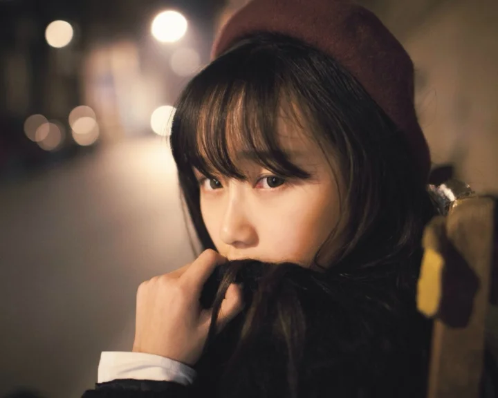 一名戴贝雷帽、裹着围巾的黑发女子在暖色虚化灯光前回望镜头。