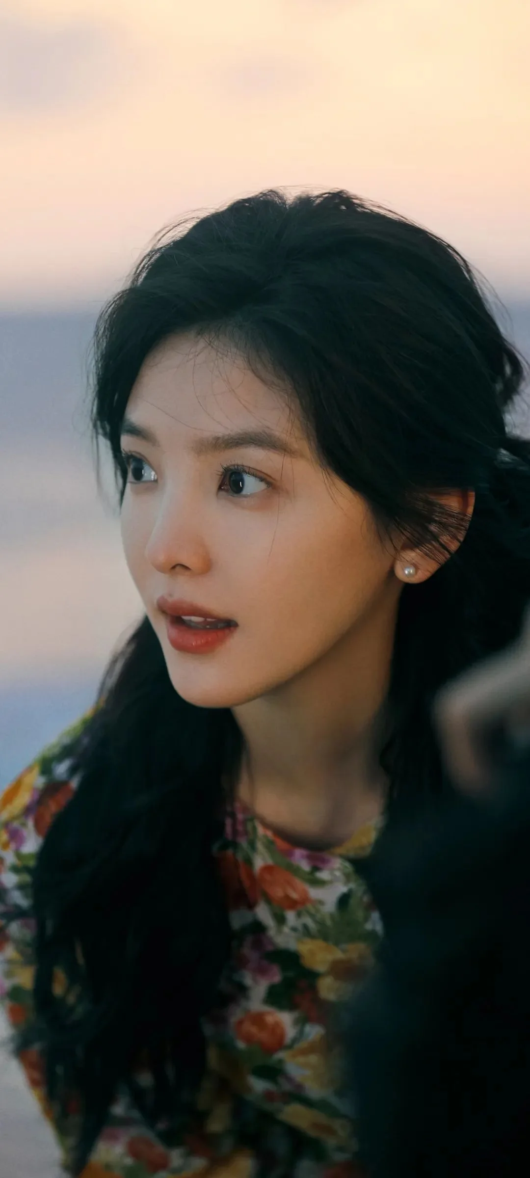 꽃무늬 옷을 입은 성인 여성이 부드럽게 흐린 배경 앞에서 옆을 바라보고 있습니다.