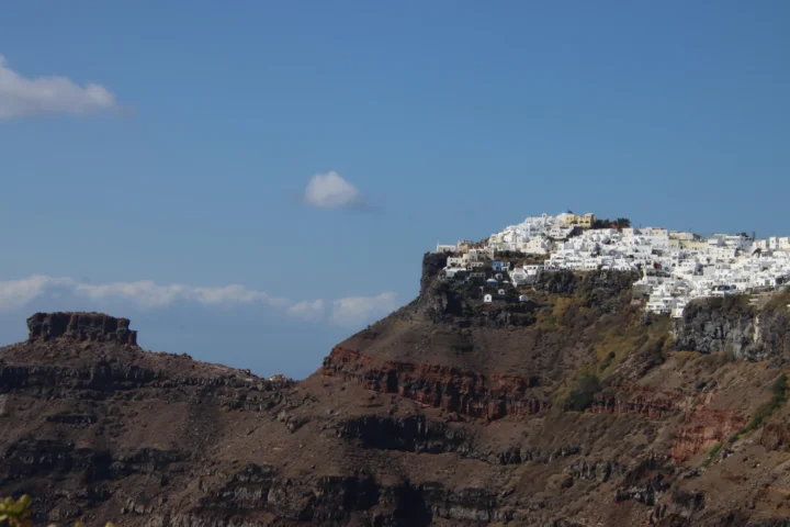 白色建筑群坐落在深色火山悬崖之上，远处是晴朗的蓝天。