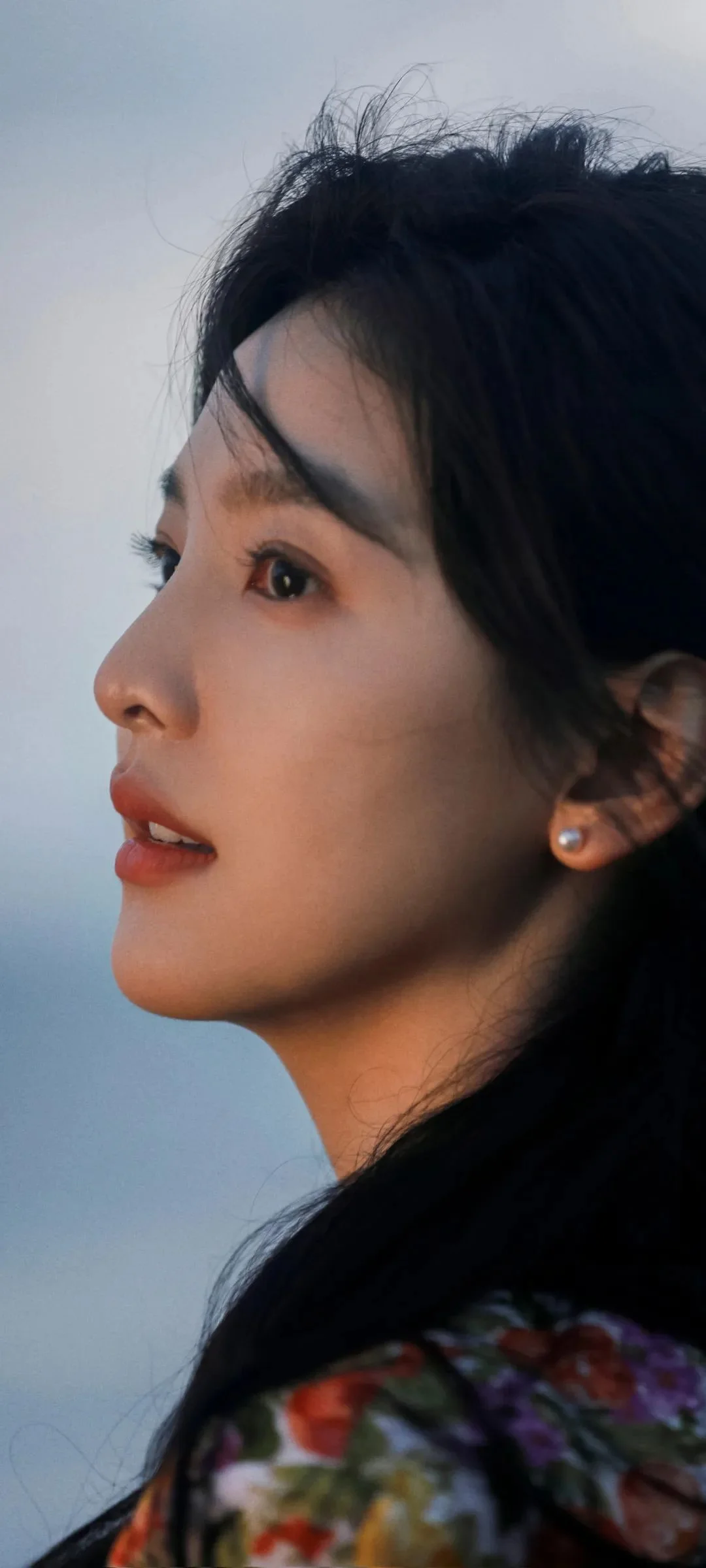 짙은 색의 긴 머리와 화려한 무늬의 옷을 입은 성인 여성의 옆모습 클로즈업입니다.
