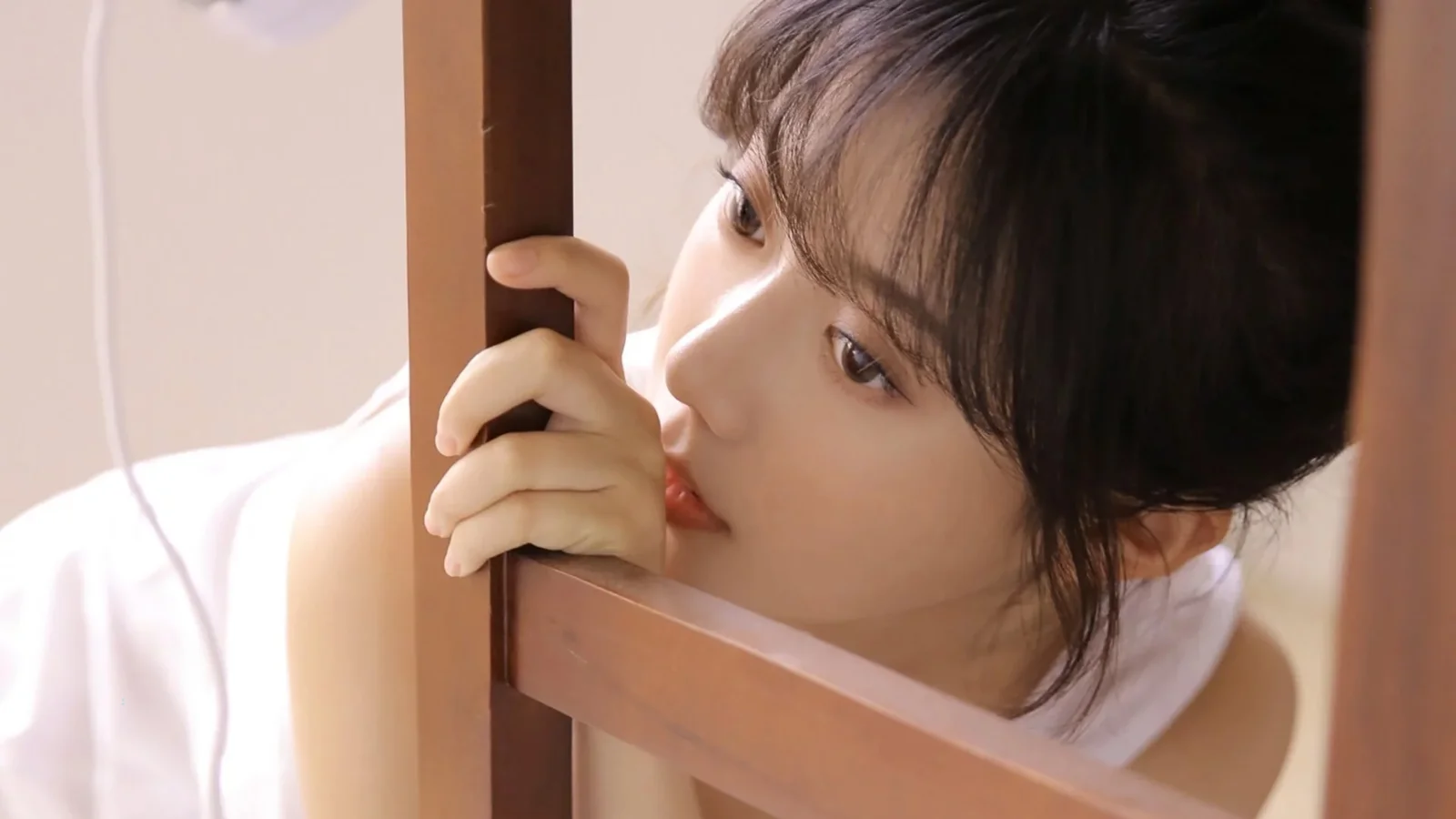 한 여성이 나무 프레임에 기대어 틈 사이로 바라보고 있다.