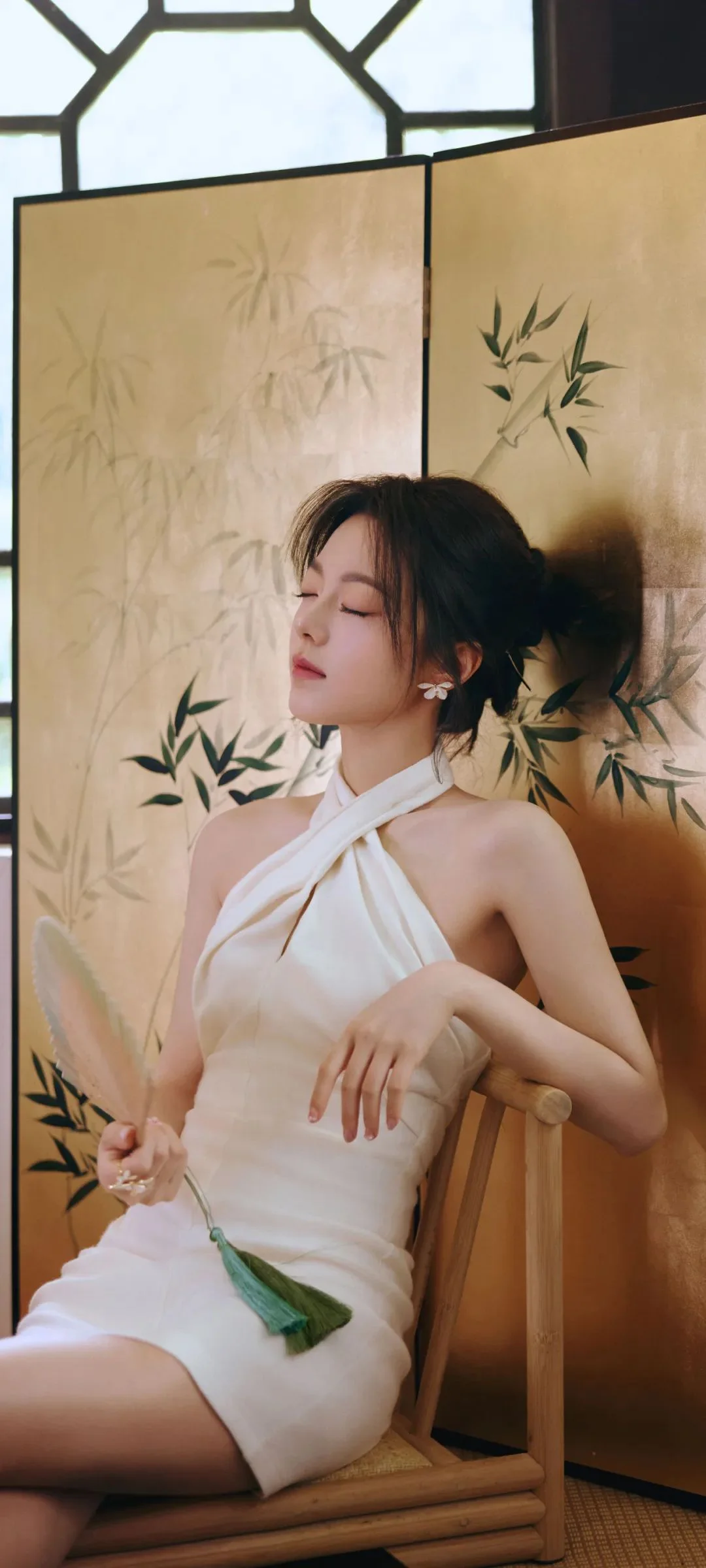 흰색 드레스를 입은 여성이 대나무 무늬 병풍 앞에 앉아 있습니다.