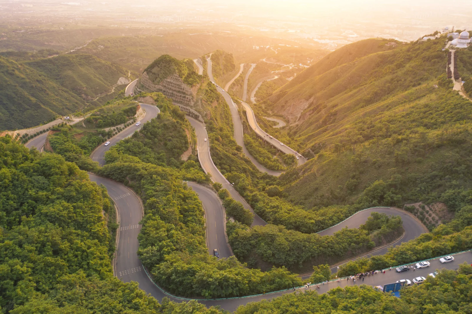 夕阳映照下，绿色山坡间蜿蜒交错的盘山公路延伸向远方。