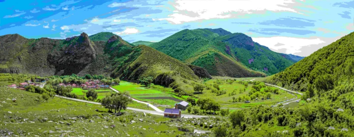 青翠群山环绕着山谷中的村庄、农田和蜿蜒道路，天空晴朗明亮。