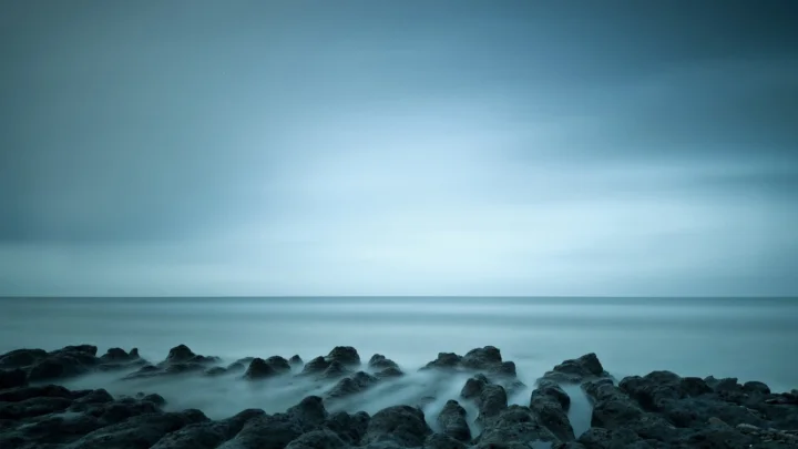 蓝色调的海面与雾化水流环绕着前景中的黑色礁石海岸。