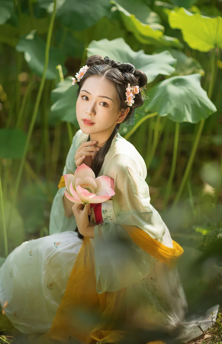 一位身穿传统服饰的女子在荷叶与荷花间手捧一朵盛开的莲花。