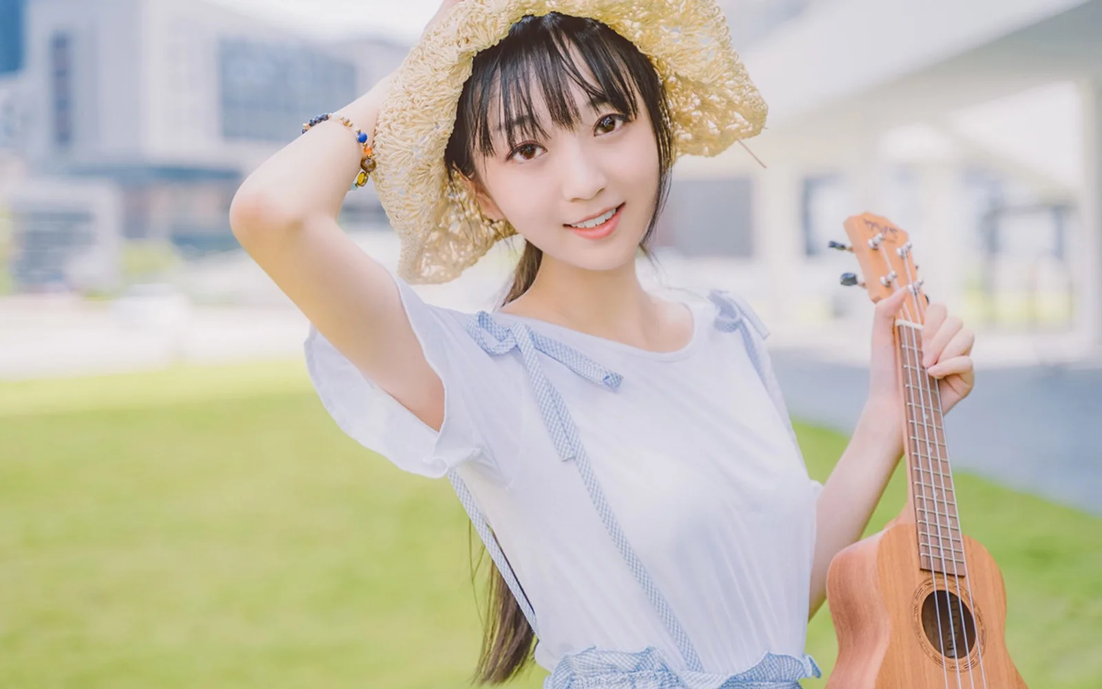 麦わら帽子と白い服を身につけた女性が、屋外の芝生でウクレレを持っています。