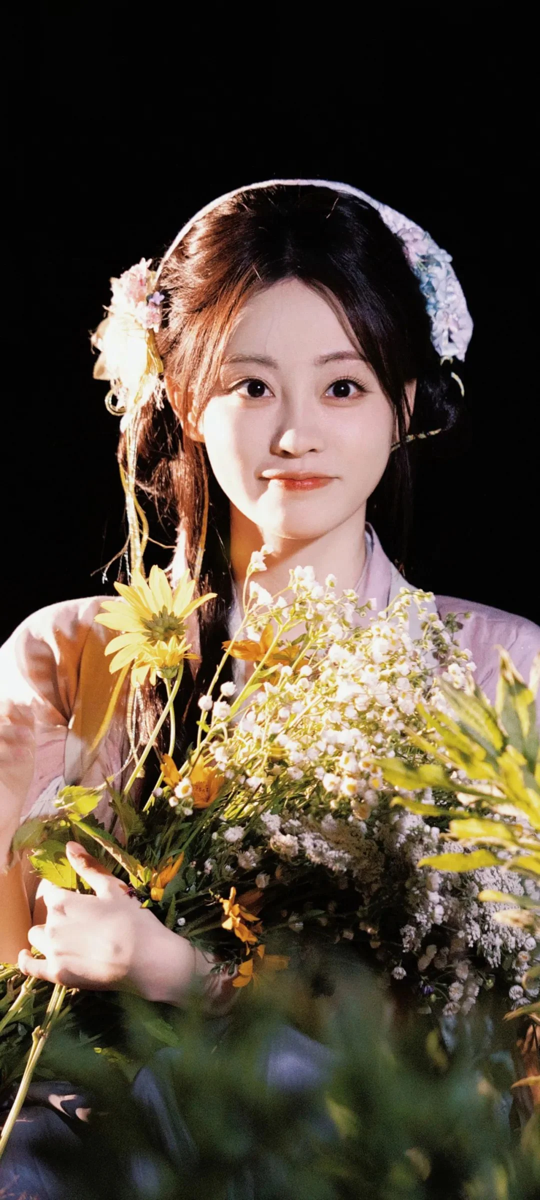 一位女子在黑色背景前手捧一大束鲜花。