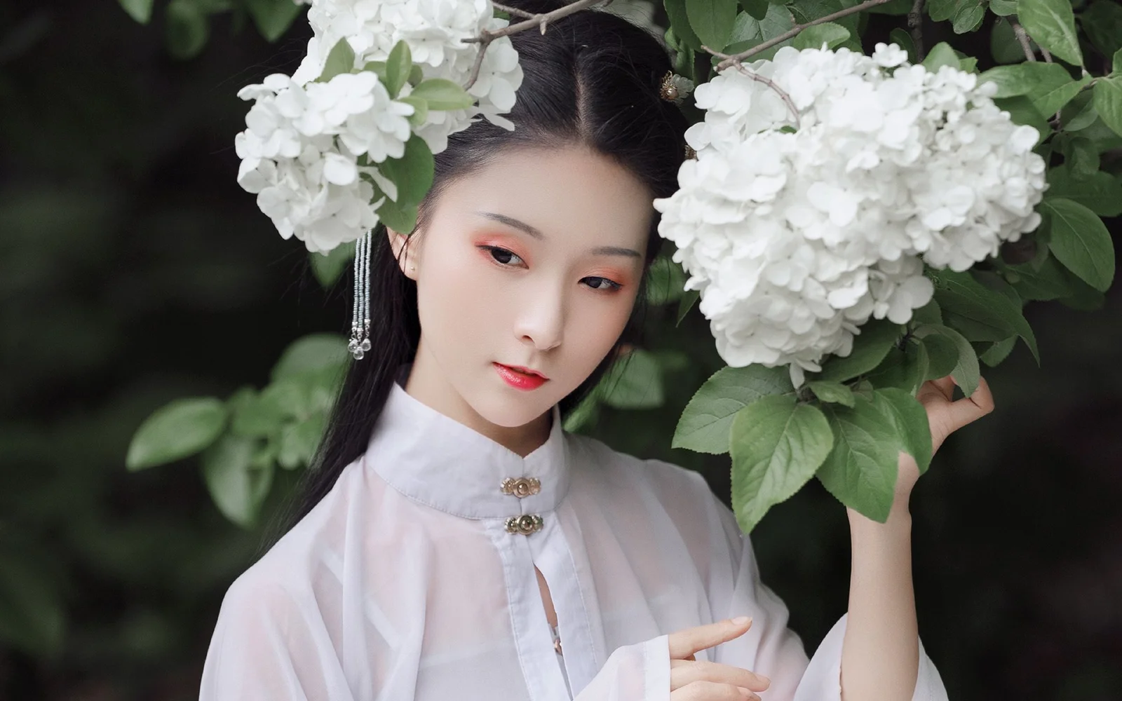 緑の葉と白い花の房に囲まれた成人女性を写した、柔らかなポートレートです。