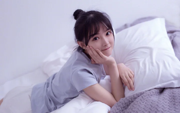 一名年轻女性趴在床上，手托脸颊望向镜头。