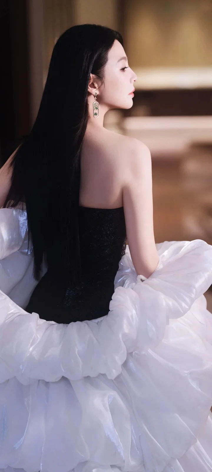 一名成年女性身穿黑色上衣和蓬松白裙，以侧身背影姿态坐在室内。