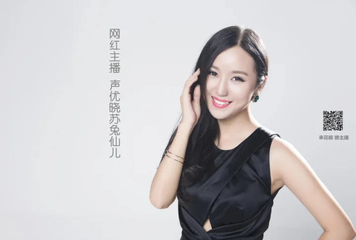 一名微笑的成年女性穿着黑色连衣裙，站在浅灰色背景前。