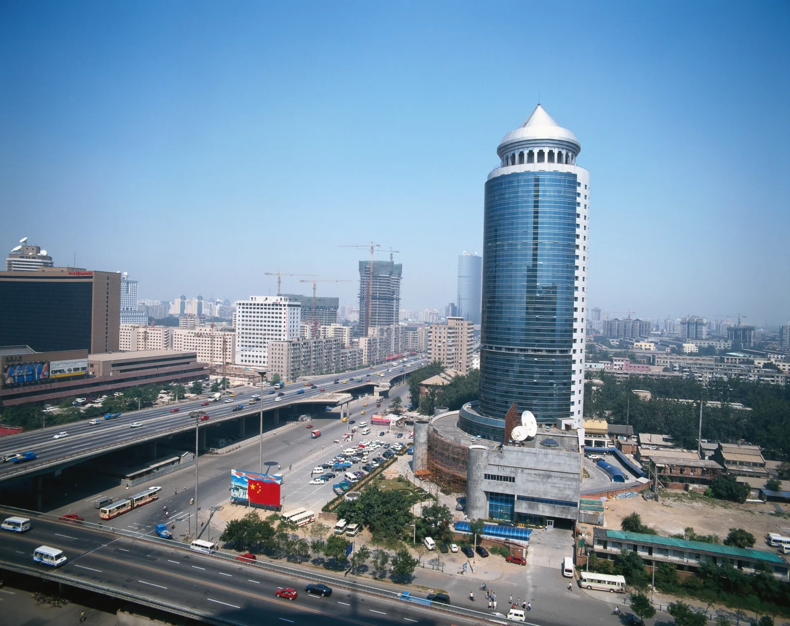 晴朗蓝天下，高架道路、城市建筑群和一座圆顶摩天大楼构成城市景观。