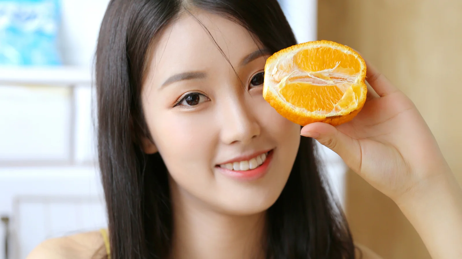 미소 짓는 성인 여성이 반으로 자른 오렌지로 한쪽 눈을 가리고 있습니다.