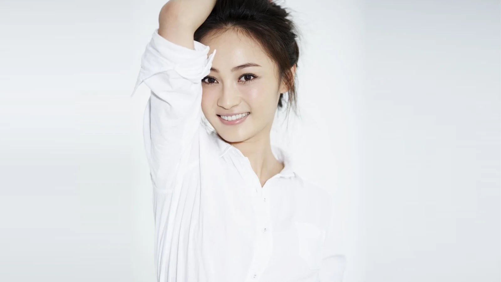 白いシャツを着た女性が片腕を上げ、カメラに向かって微笑んでいる。