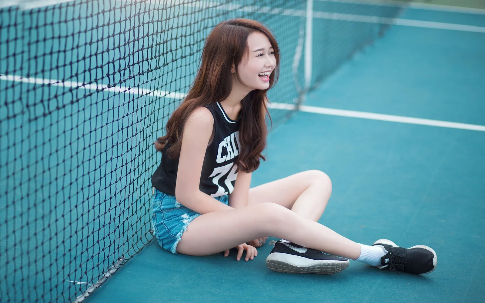 한 젊은 여성이 스포츠 코트의 네트 옆에 앉아 있습니다.