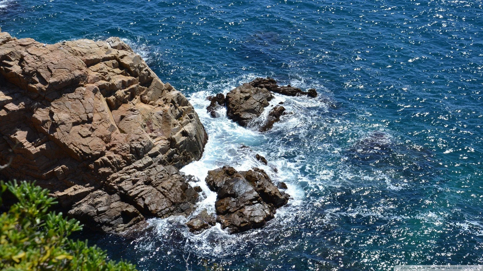 阳光下的蓝色海水拍打着崎岖的岩石海岸。