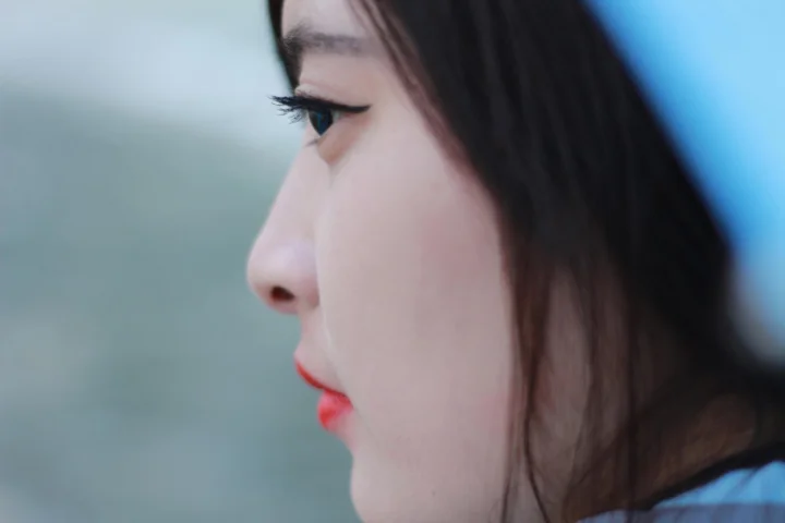 一名成年女性的侧脸特写，带有黑色长发、眼线和红色唇妆。