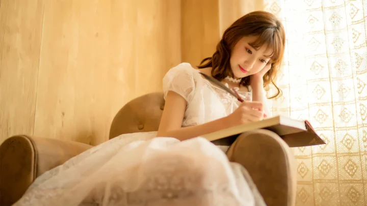 한 여성이 실내 안락의자에 앉아 커튼 사이로 들어오는 햇빛 속에서 책을 읽고 있다.