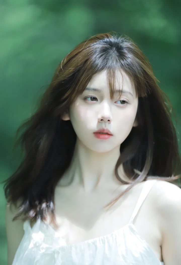 一位长发女性身穿白色上衣，在绿色虚化背景前的肖像照片。