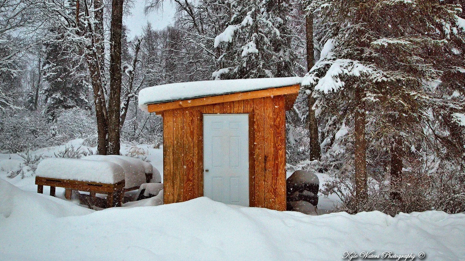 积雪覆盖的森林中，一座木制小屋被厚厚的白雪包围。