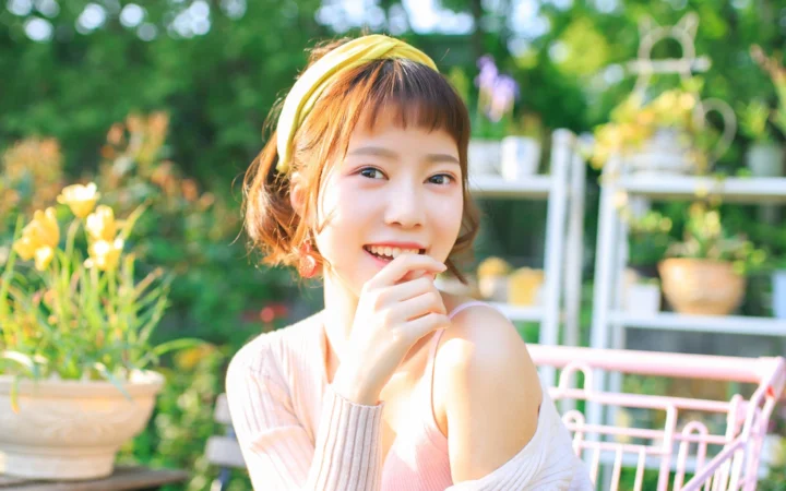 노란색 헤어밴드를 착용한 성인 여성이 햇살이 비치는 정원에서 미소 짓고 있다.