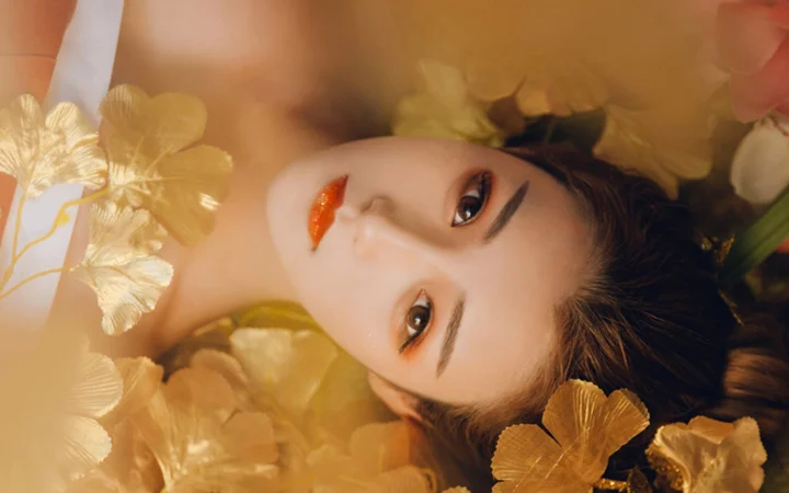 一位成年女性的面部特写被金色花朵环绕，呈现温暖柔和的妆容与光影。