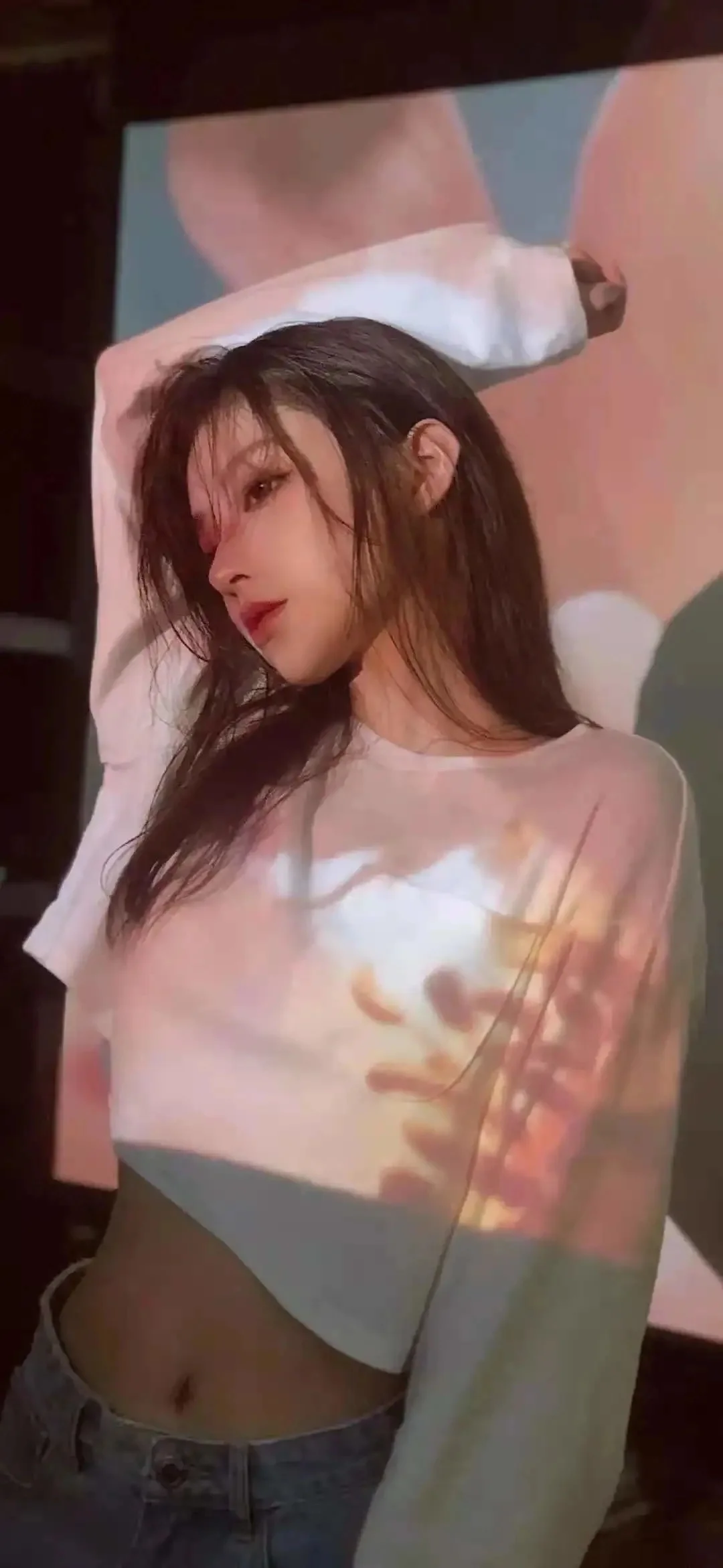 긴 머리의 여성이 밝은 색상의 긴소매 상의를 입고 부드럽고 다채로운 프로젝션 빛을 받고 있습니다.