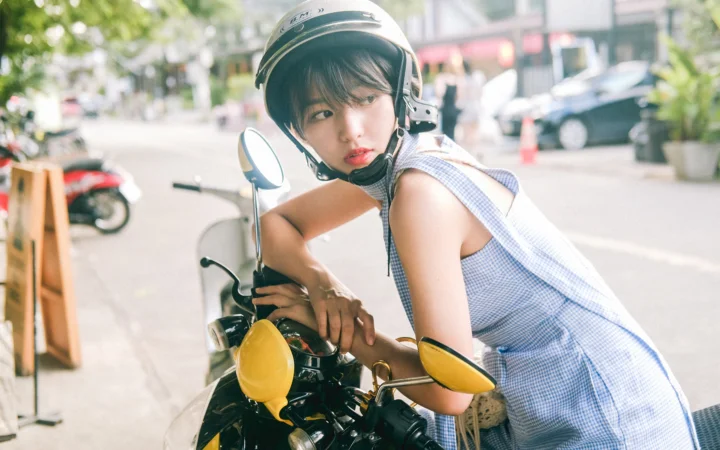 一名戴着头盔的女子坐在街边的摩托车上回头看向镜头。