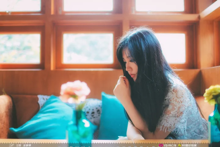 한 여성이 나무 창문 옆 소파에 앉아 따뜻한 햇빛이 실내로 들어오고 있다.