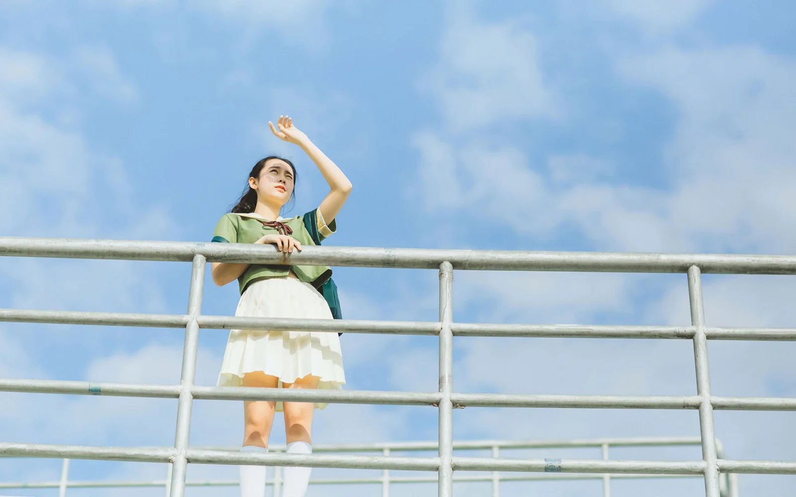 青空と雲の下で、女性が手すりのそばに立っています。