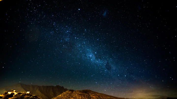 璀璨的银河横跨深蓝色夜空，地平线下方隐约可见崎岖山脉。