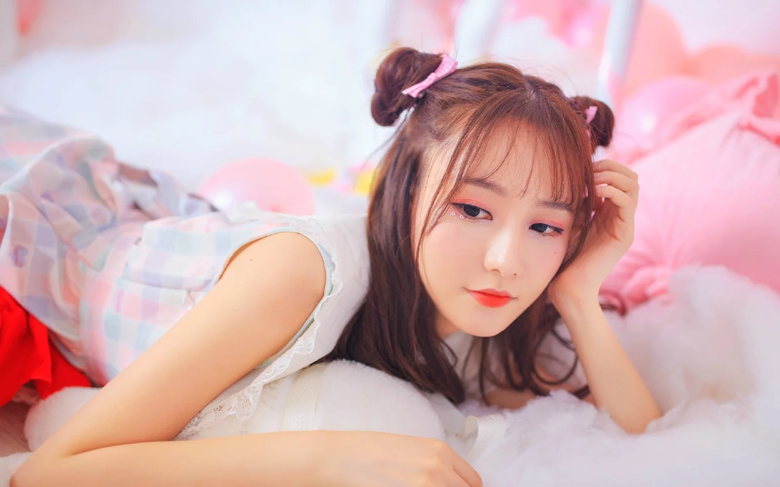 한 여성이 부드러운 흰색 침구 위에 누워 분홍색 배경과 폭신한 장식에 둘러싸여 있다.