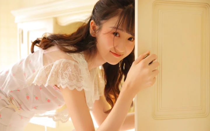 一名成年女性穿着白色蕾丝上衣，在暖色室内门旁回头微笑。