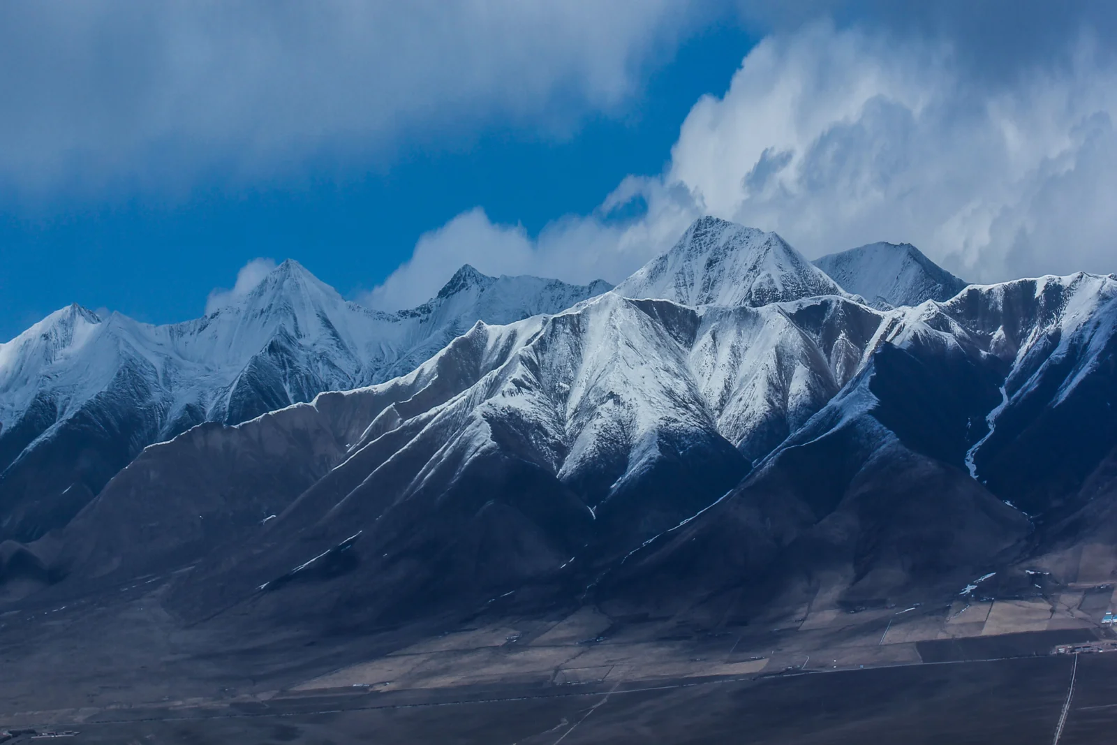 画面展现了被云层环绕的连绵雪山和山脚下的深色山谷。